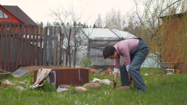 Молодой человек собирает камни во дворе — стоковое видео