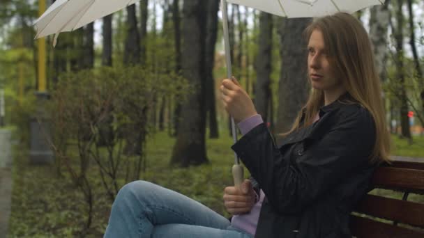 Серьезная женщина с зонтиком сидит на скамейке — стоковое видео