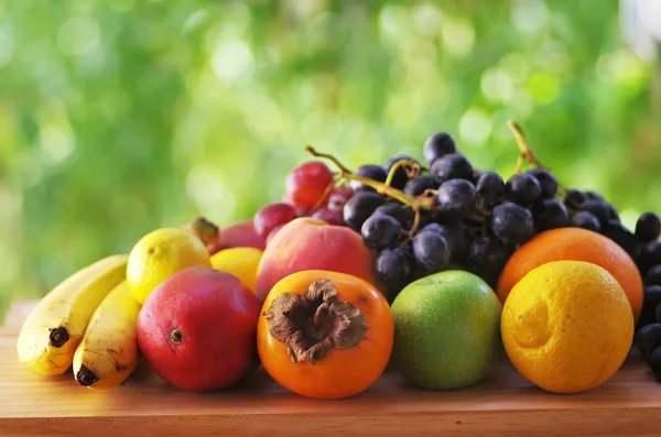 Auswahl an reifen Früchten auf Holztisch, grüner Hintergrund — Stockfoto