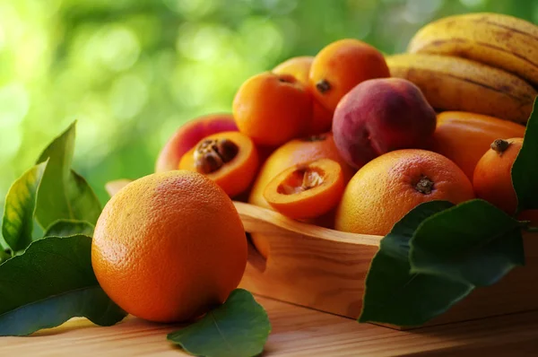 Спелые апельсины и различные фрукты на деревянной корзине — стоковое фото