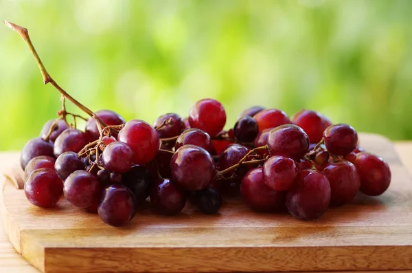 Bunch of red grapes on table, green background — Stock Photo, Image