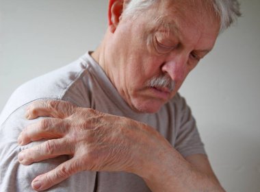 Senior man grips his shoulder in pain with room for text clipart