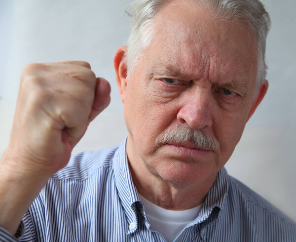 Older man holds his fist up in anger