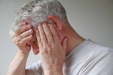 Elleri neredeyse yüzünü kaplayan kıdemli bir adam.