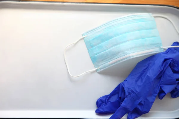 Plastic gloves and a disposable face mask on a white tray with room for text