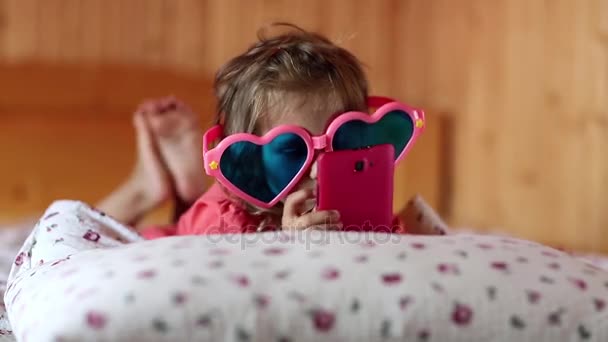 Menina com smartphone encontra-se na cama — Vídeo de Stock