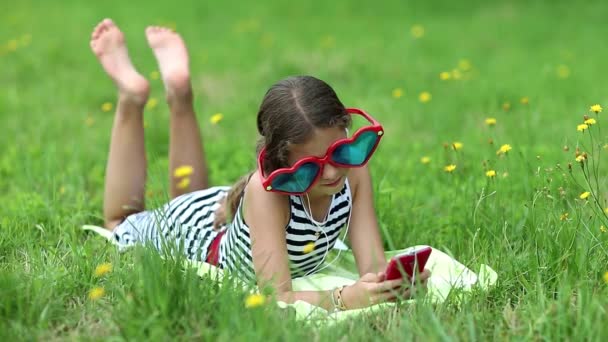 Mädchen mit rotem Smartphone liegt im Gras — Stockvideo