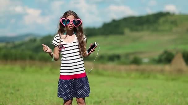 スマート フォンを持つ少女が牧草地の上に立つ — ストック動画