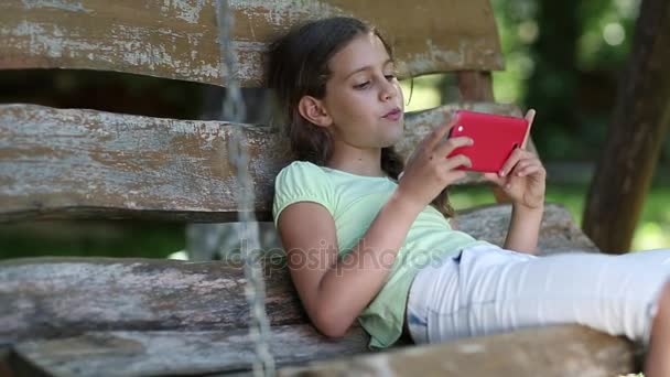 Girl with smartphone sits on swing bench — Stock Video