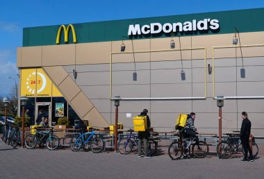 KYIV, UKRAINE, 20 Nisan 2020: Glovo bisikletli kuryeler ve McDonalds fast food restoranının yakınındaki arabalar. Covid-19 salgını sırasında restoran sadece arabalar için çalışır.