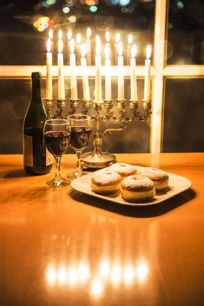Celebrating Hanukkah with Menorah (candlestick with 8 candles) by the window with the night city view — Stock Photo, Image