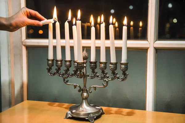 Litting up Menorah (candelero con 8 velas) por la ventana con la vista de la ciudad de noche —  Fotos de Stock