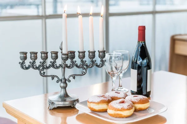Hanukkah - jewish holiday of light with menorah and bottle of red wine with two glasses by the window — Stock Photo, Image