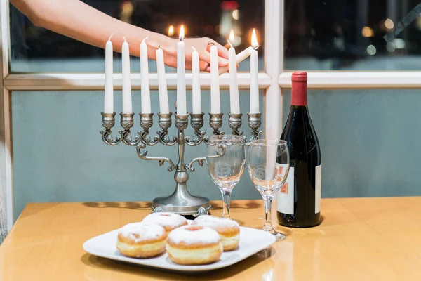 Litting up Menorah (candlestick with 8 candles) by the window with the night view on city — Stock Photo, Image