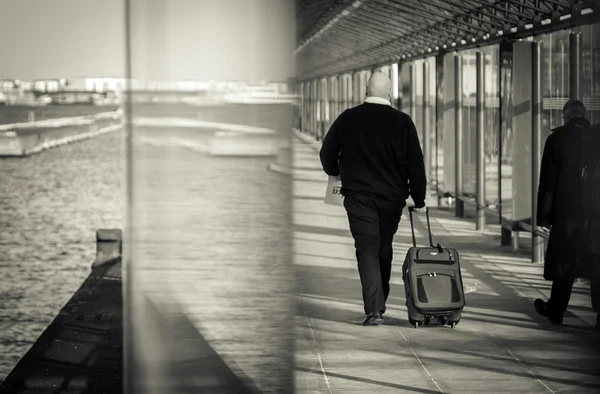 Man with a luggage walking through glass tunnel.