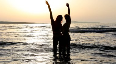 Yazın kumsalda gün batımının romantik manzarasında aşık çiftlerin silueti.