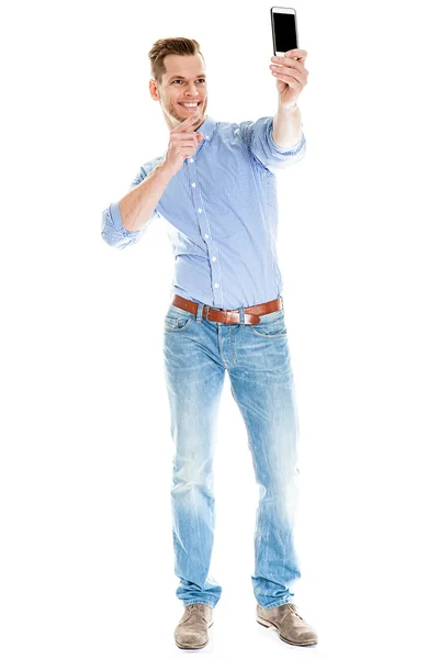 Selfie Photo - Full length portrait of a young man taking a selfie with his smart phone, isolated on white background Stock Picture