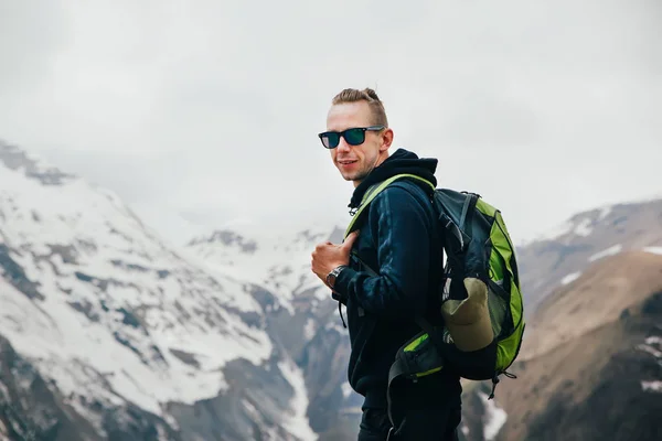 Молодой человек с рюкзаком стоит на вершине горы — стоковое фото