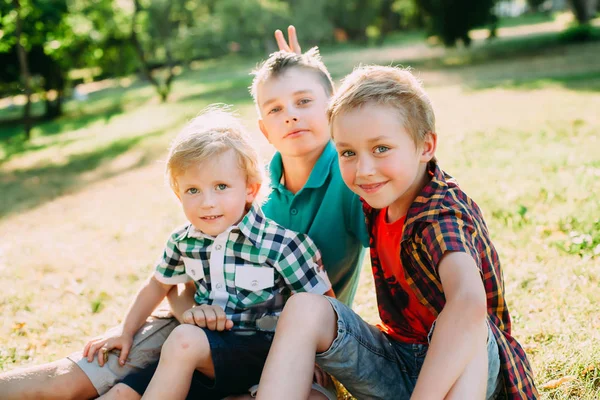 Retrato exterior de tres felices hermanos al atardecer. Los chicos posan y miran a la cámara — Foto de Stock