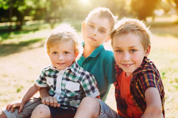 Retrato exterior de tres felices hermanos al atardecer. Los chicos posan y miran a la cámara — Foto de Stock