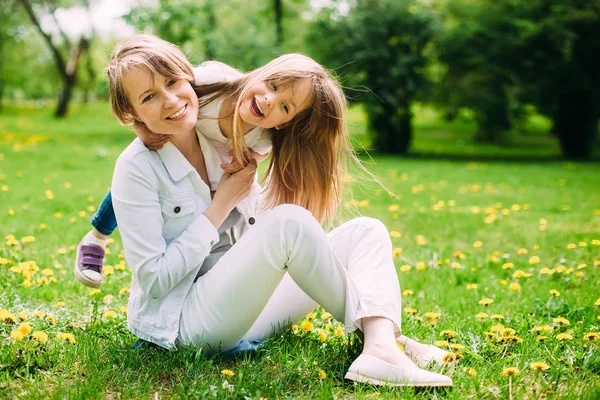 Hugging happy mother and daughter for a walk in the park On the green lawn — Stock Photo, Image