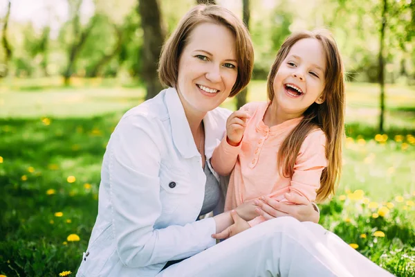 Abrazando feliz madre e hija para un paseo en el parque en el césped verde — Foto de Stock