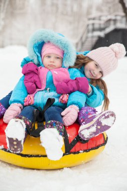 Küçük kız kardeşler kışın tepelerden kar tüneline binerler.