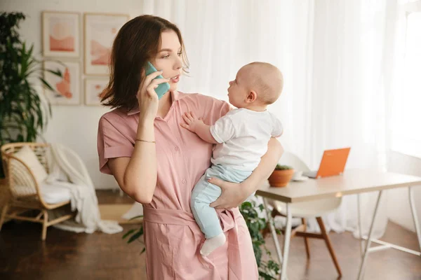 Une jeune mère tient un bébé dans ses bras et parle au téléphone — Photo