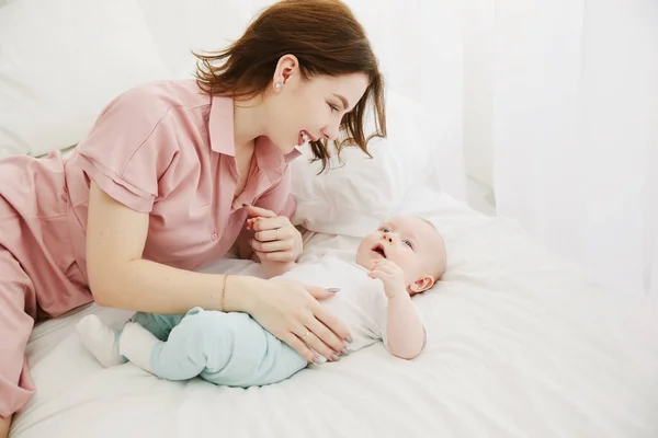 Portrait of happy young mother and baby lying on the bed at home — Stock Photo, Image