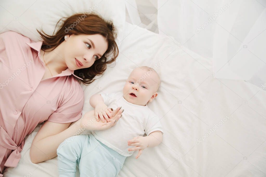 Portrait of a young beautiful caucasian mom and baby on the bed. Top view. Copy space