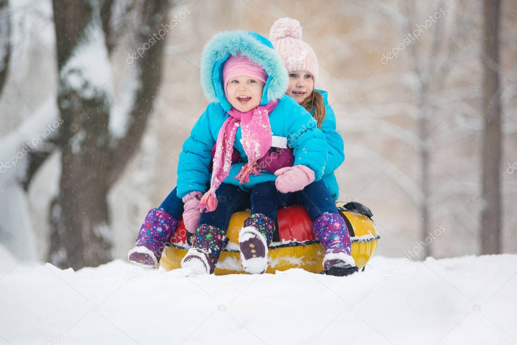 Little girls ride a snow tube. Winter holidays, holiday for children in winter. Winter city park