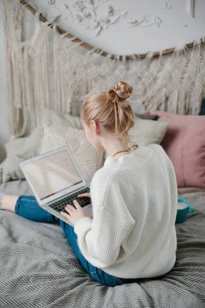 Kvinna med blont hår skickar sms från laptop medan du dricker kaffe. Ung kvinna bestämde sig för att stanna hemma — Stockfoto