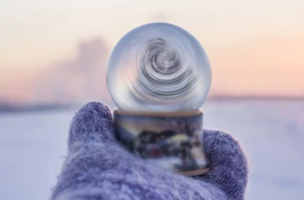 Meisje in gebreide wanten houden van glazen bal met betoverende swirl binnen de bal met winterlandschap op de achtergrond — Stockfoto