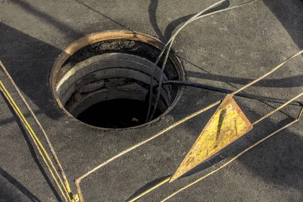 Disposición del cable en un pozo de alcantarillado en la carretera asfaltada rodeada por barandillas que muestran señal de atención — Foto de Stock