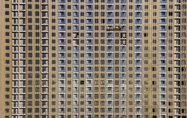 Будівельні оздоблювальні роботи фасаду будівельниками в будівлі колиски нових житлових будинків і баштових кранів — стокове фото