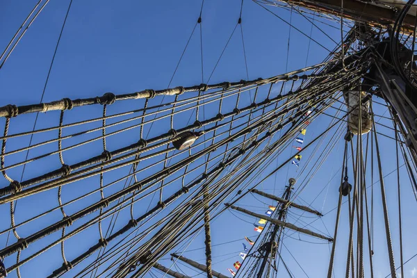 Nautical part of a yacht or a big old sailing ship with cords, rigging, sail, masts, knots, signal flags in front of a blue sky — Stock Photo, Image