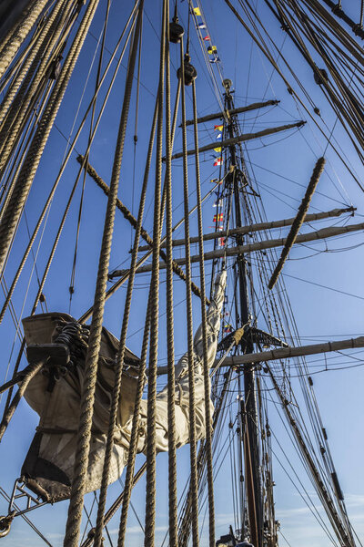 Nautical part of a yacht or a big old sailing ship with cords, rigging, sail, masts, knots, signal flags in front of a blue sky