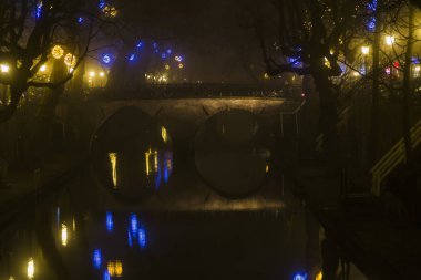  Utrecht, Hollanda, 21 Ocak 2020. Utrecht 'in merkezindeki kanal boyunca çift yay taş köprü. Misty Evening, kanalın gece manzarası, eski Hollandalı evler, kanal boyunca bisikletler.