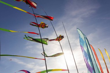 Renkli kurdeleler ve uçurtma figürleri kutuplarda asılı ve mavi gökyüzü arka plan uçurtma festivalinde uçuyor.