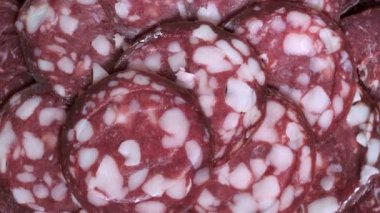 Bir tabağa tütsülenmiş sosis dilimleri konmuş, bakkal arka planında dönen et videosu yukarıdan makro çekim