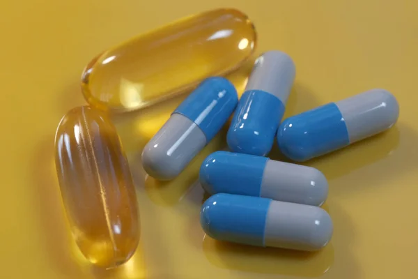 Yellow gelatin soluble capsules with vitamin omega three and blue on a yellow background close-up macro photo