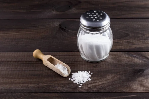 Salt with wooden spoon and glass saltshaker on wooden table — Stock Photo, Image