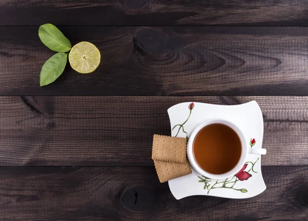 Cup of tea with tea cookies and fresh lime on wooden table — Stock Photo, Image