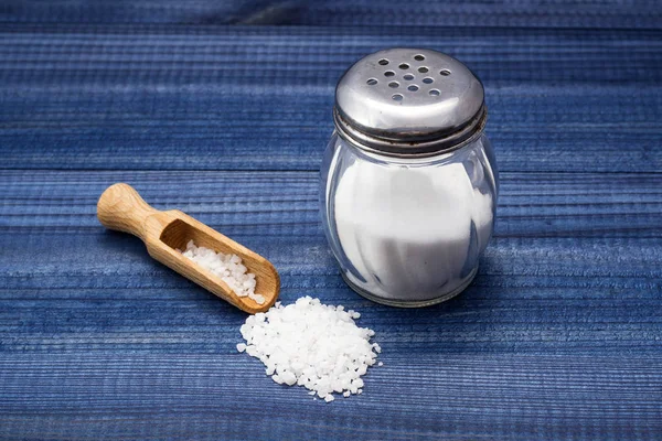 Zoutkristallen met houten lepel en glas zout shaker op blauwe houten tafel — Stockfoto