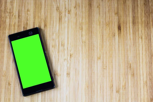 Smart phone with green screen on wooden desk — Stock Photo, Image