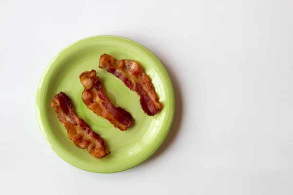 Três pedaços de bacon em uma placa verde isolado em um branco Backg — Fotografia de Stock