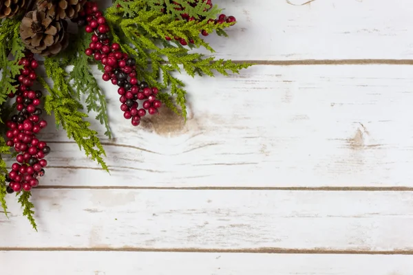 Рождественская гирлянда с шишками и ягодами на деревянной доске — стоковое фото