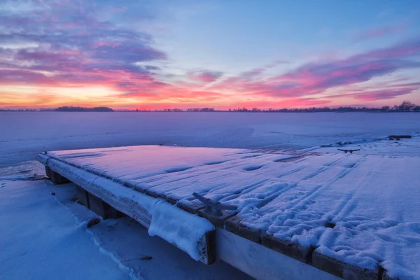 雪の冬の日の出は、湖と釣りドックを覆われています。 — ストック写真