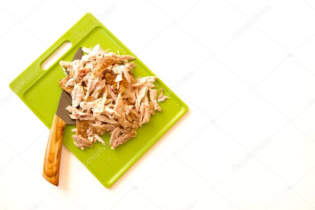 Shredded rotisserie chicken on a green cutting board and carving