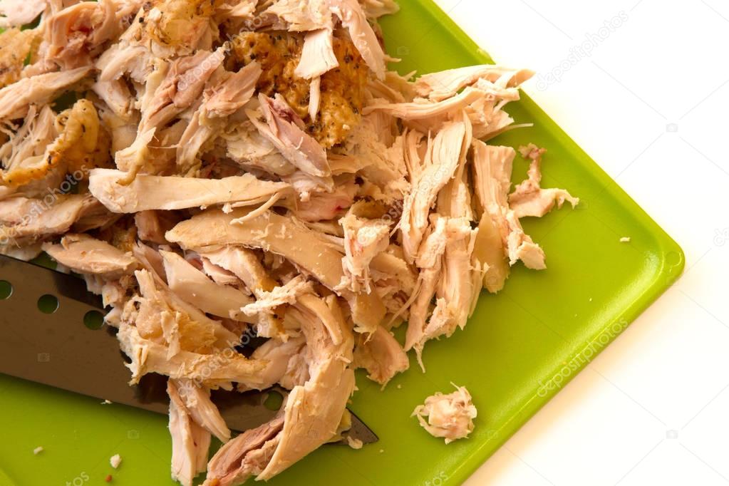Shredded rotisserie chicken on a green cutting board and carving